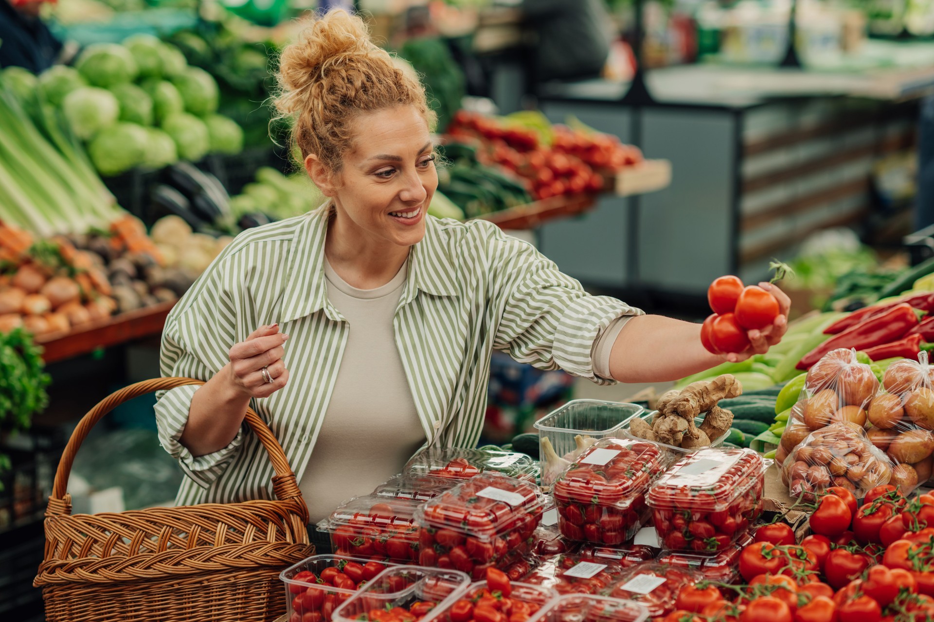 Smiling shopper woman choosing fresh tomatoes at farmers market.